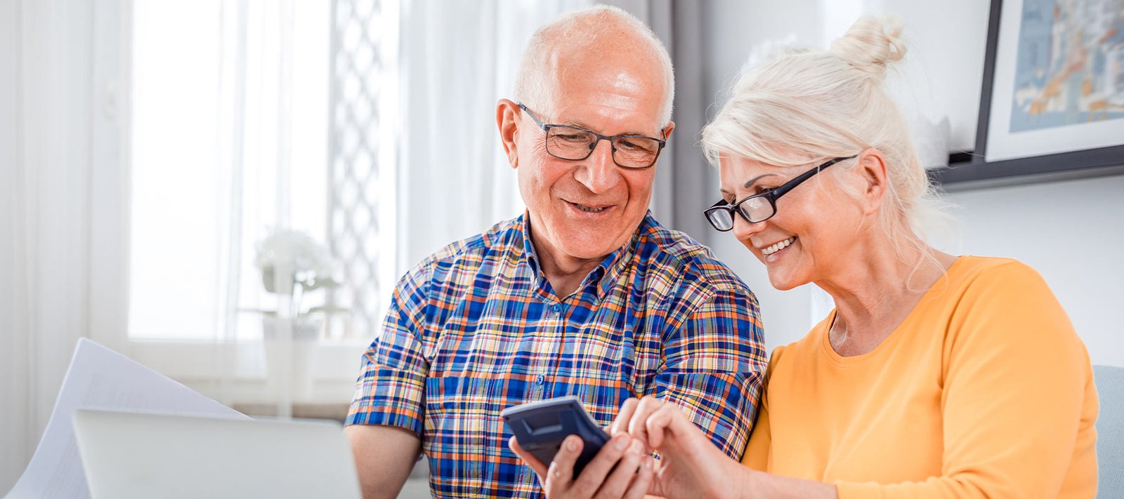 Couple de seniors souriants préparant ensemble leur budget dans un intérieur lumineux
