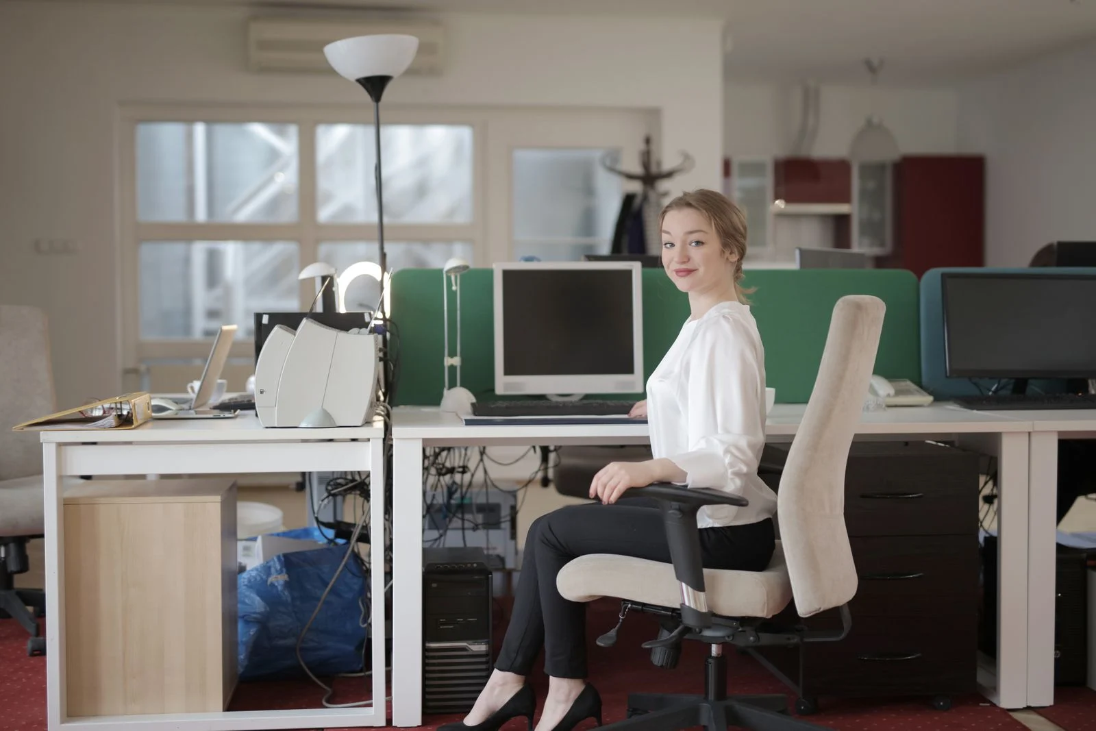 Mutuelle Entreprise Collective : Side view of glad female worker in classy outfit sitting at table on office chair during work in modern workplace and looking at camera
