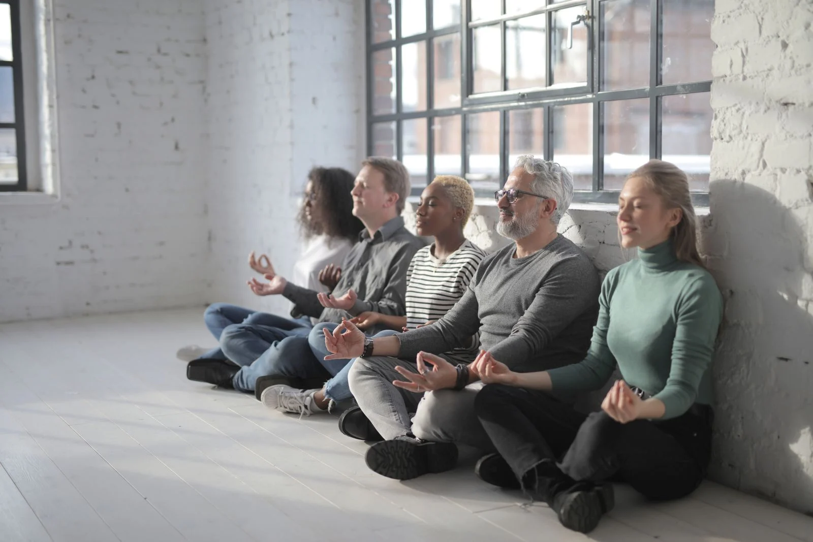 Mutuelle Entreprise Collective : Concentrated multiethnic group of coworkers sitting on floor and having break and meditating all together in modern light office
