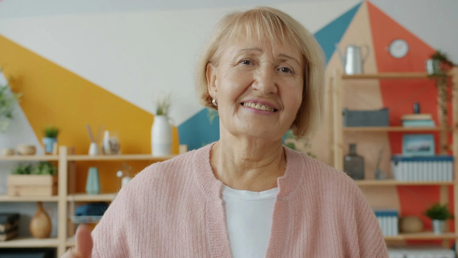 Mutuelle Sante Senior : Smiling elderly woman in a pink cardigan indoors