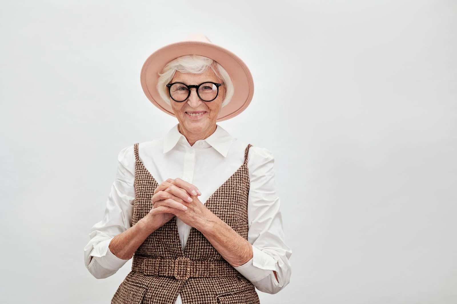 Mutuelle Sante Senior : Fashionable senior woman smiling confidently in a stylish outfit with hat and eyeglasses.