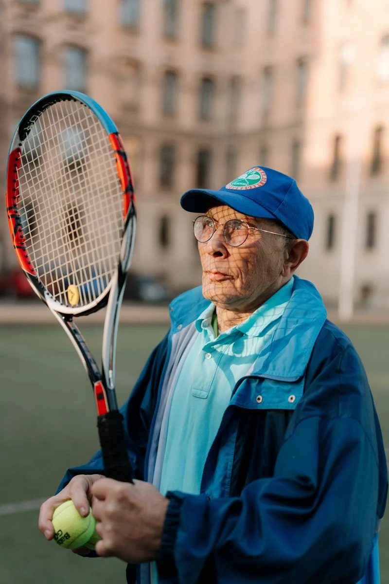 Mutuelle Sante Senior : Senior man holding a racket and tennis ball on an outdoor court.