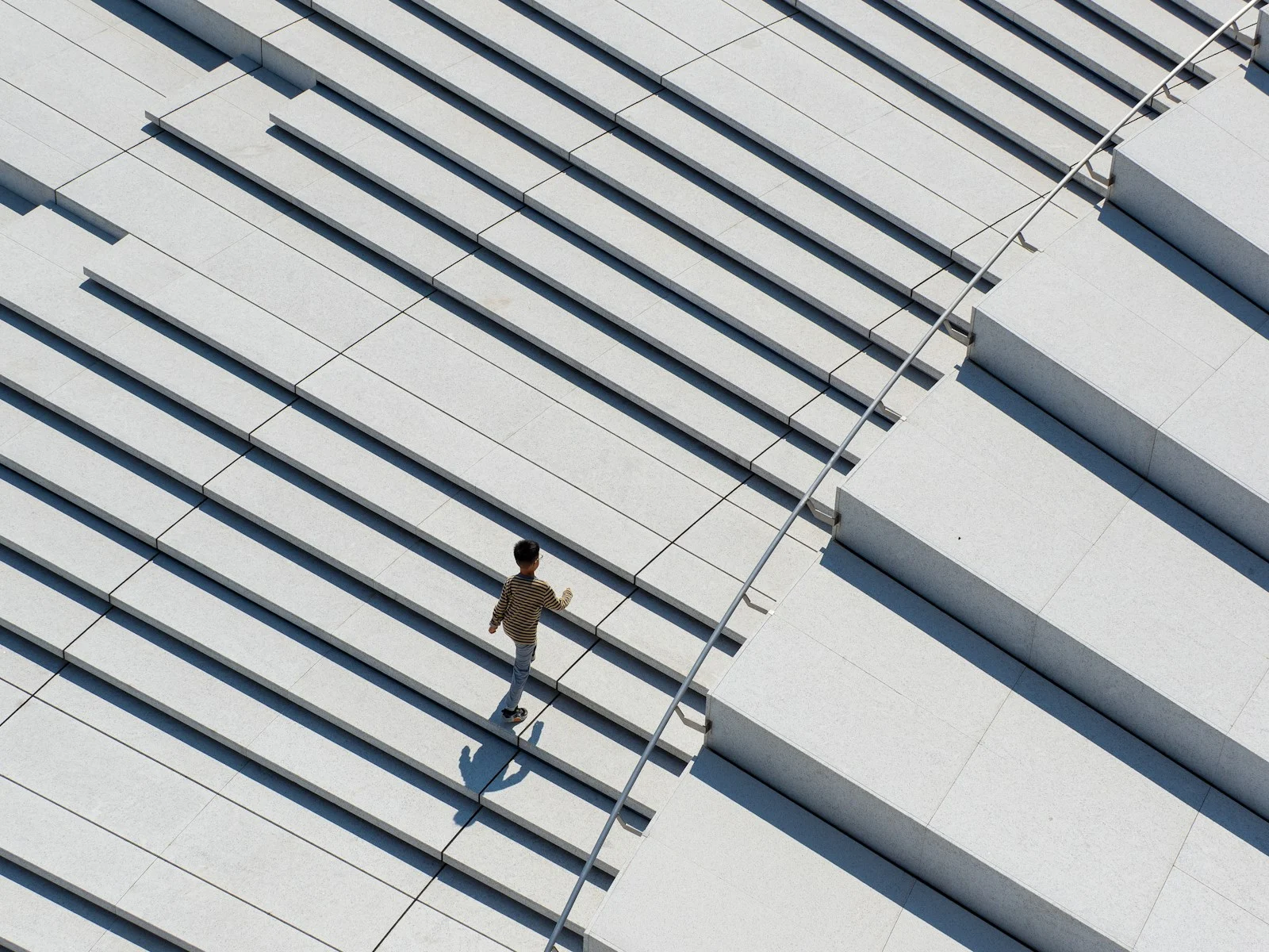 A person in a striped shirt walking up wide grey stone stairs