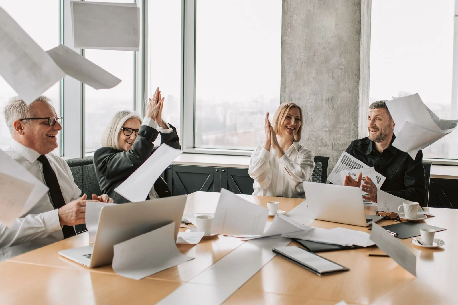 Mutuelle Entreprise Collective : Group of happy coworkers celebrating a successful meeting, throwing papers and clapping in a modern office.