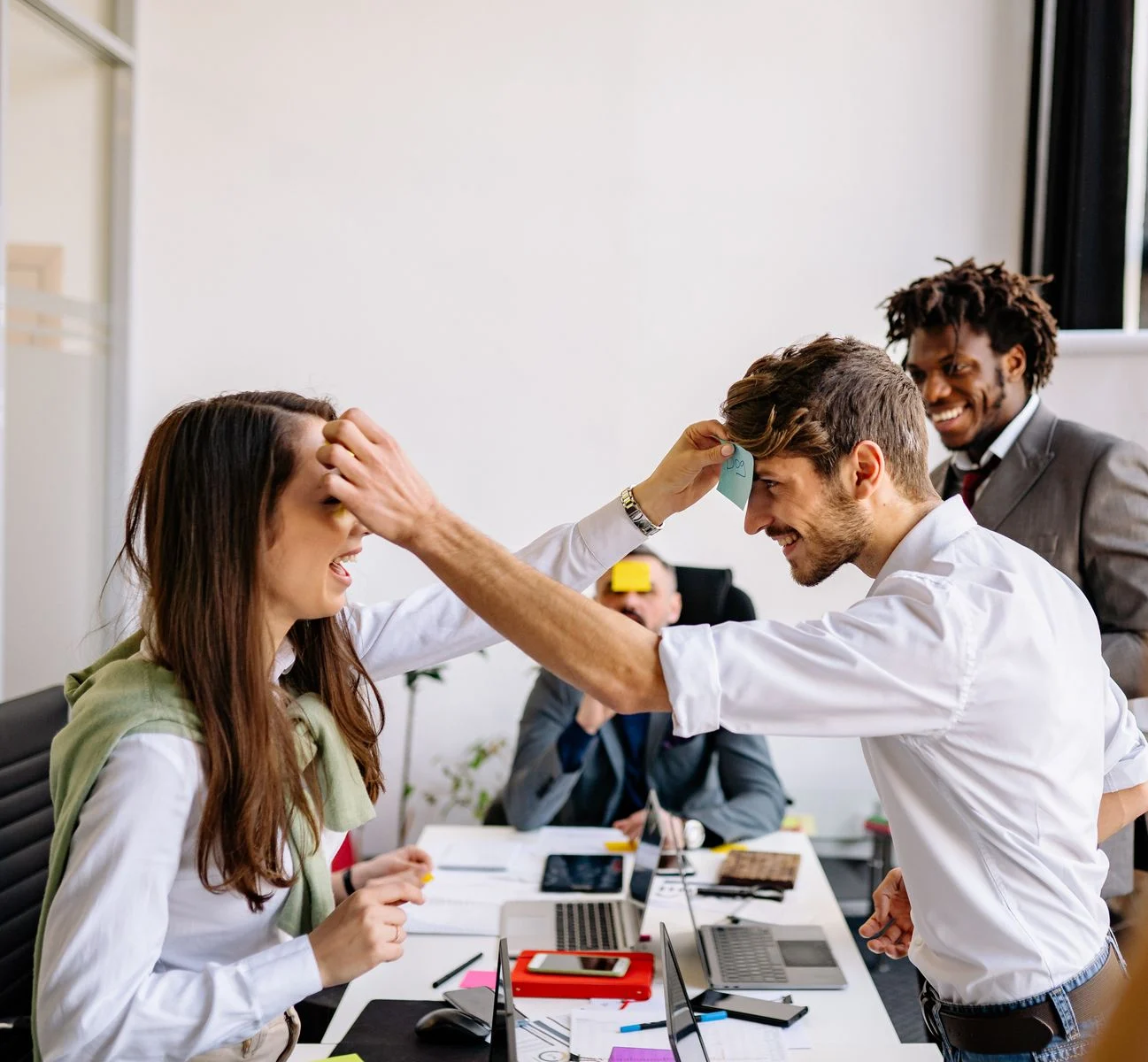 Mutuelle Entreprise Collective : Office colleagues playing a humorous sticky note game during a break, sharing laughter.
