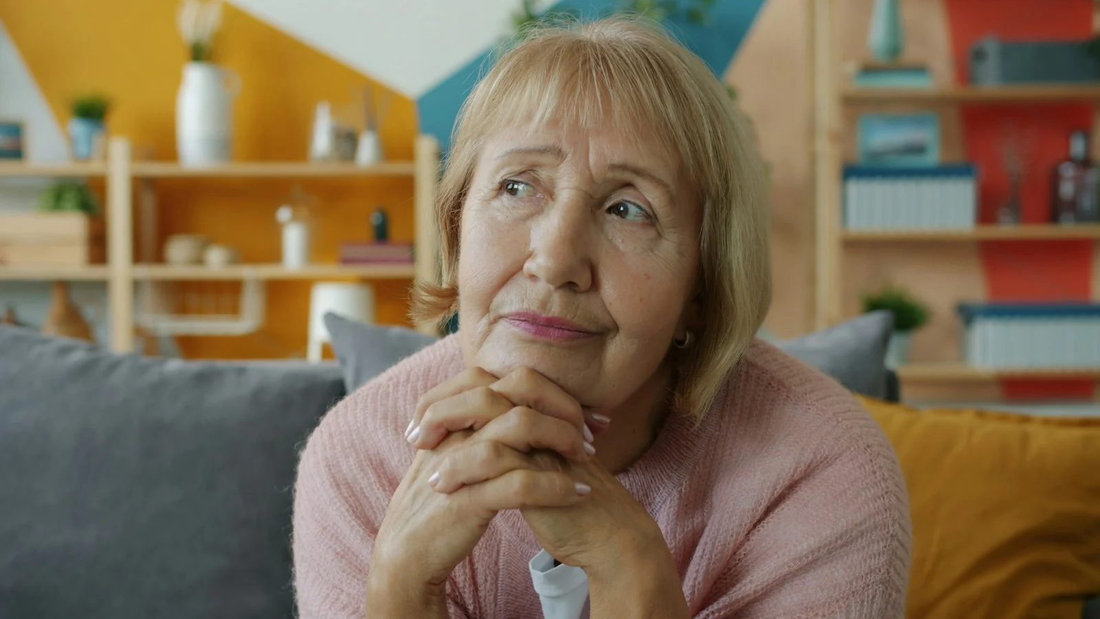mutuelle santé Elderly woman with hands clasped, looking thoughtful