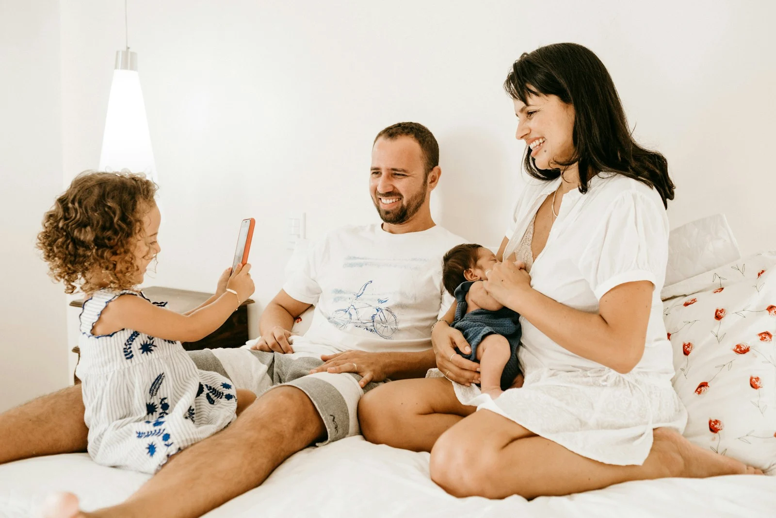 family on a bed, a child holding a phone, an adult holding a baby