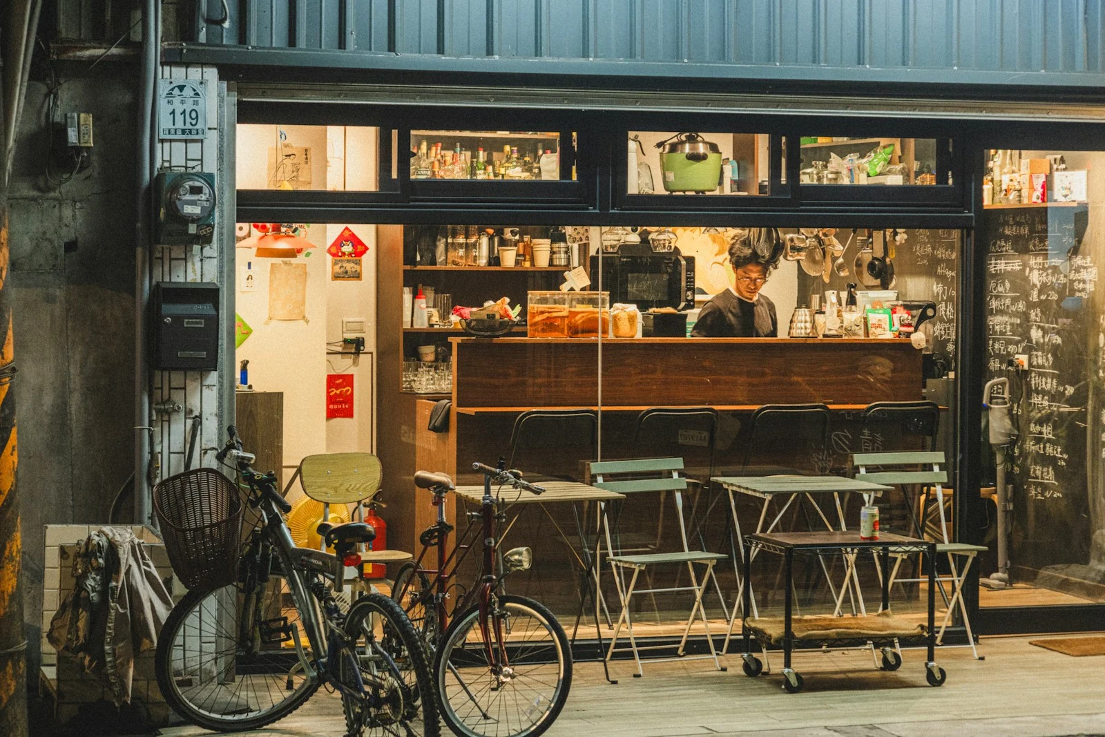TNS : A cozy cafe storefront with tables outside at night