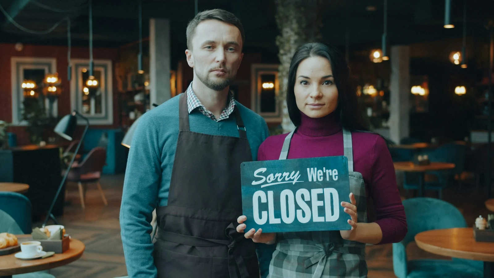 TNS : A man and woman in aprons holding a "Sorry We're CLOSED" sign
