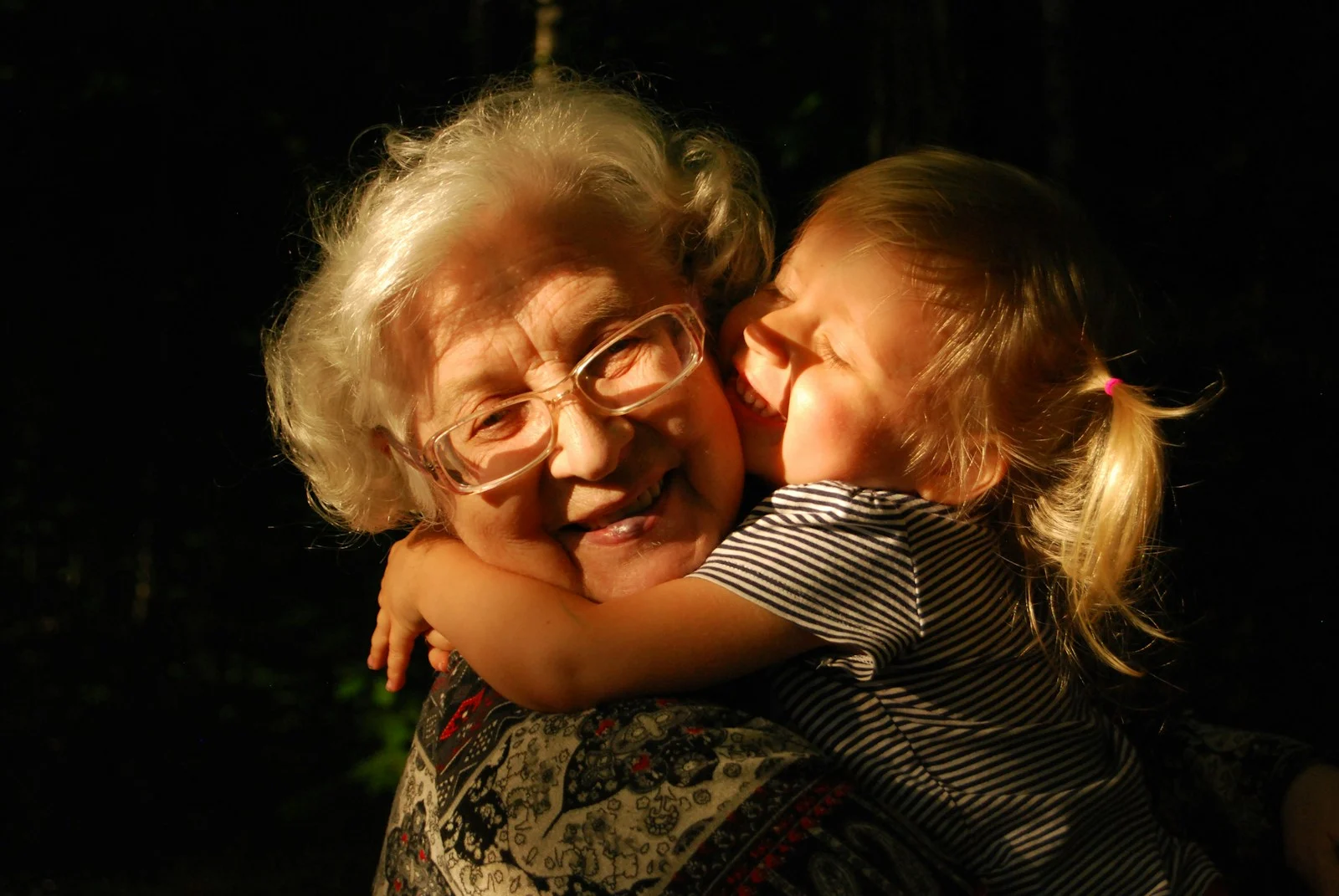 Family An elderly woman with white hair and glasses hugging a young child