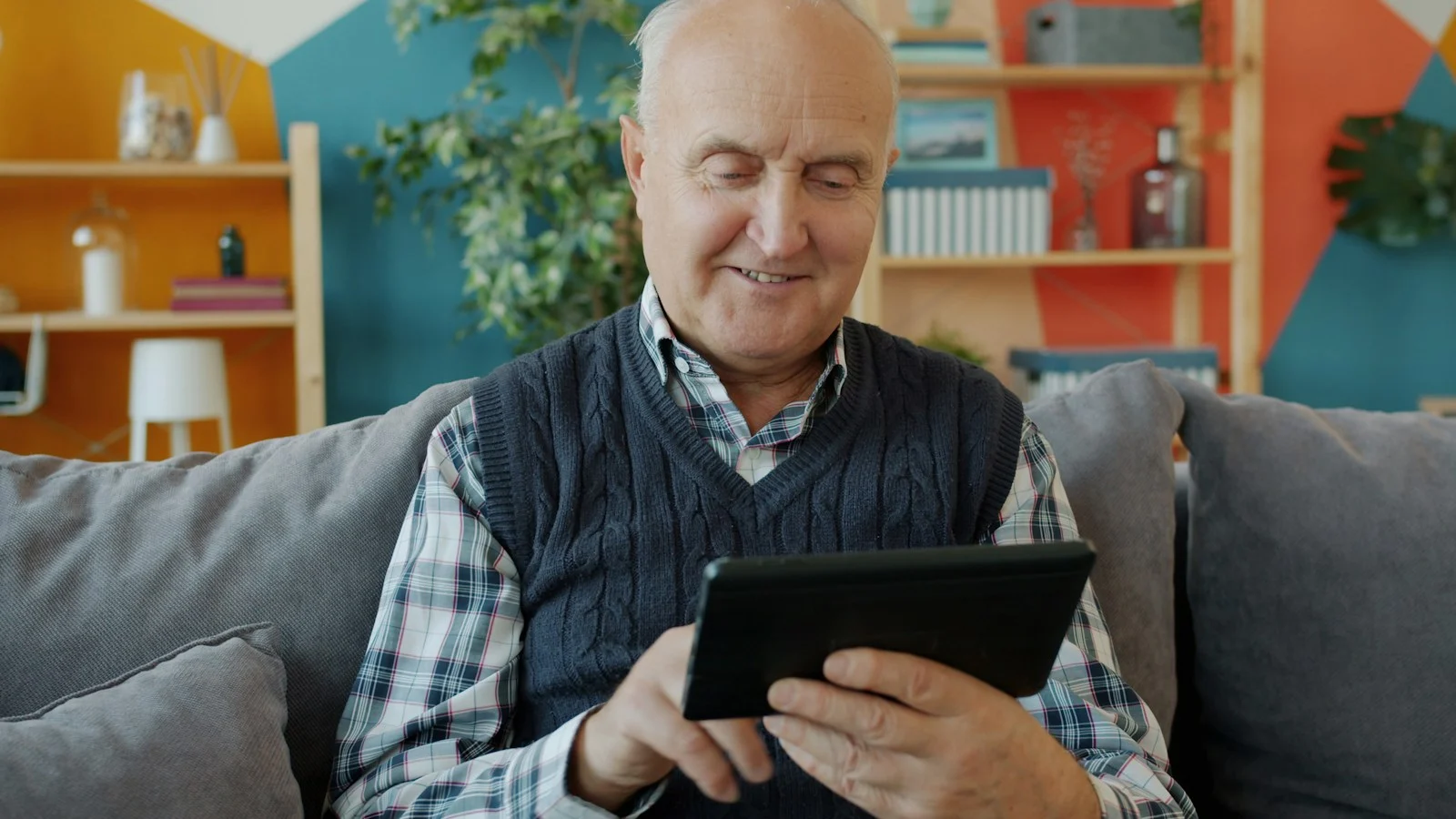 Homme âgé souriant utilisant une tablette sur un canapé