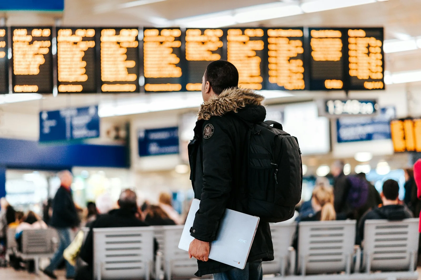 Expatrie : man standing inside airport looking at LED flight schedule bulletin board