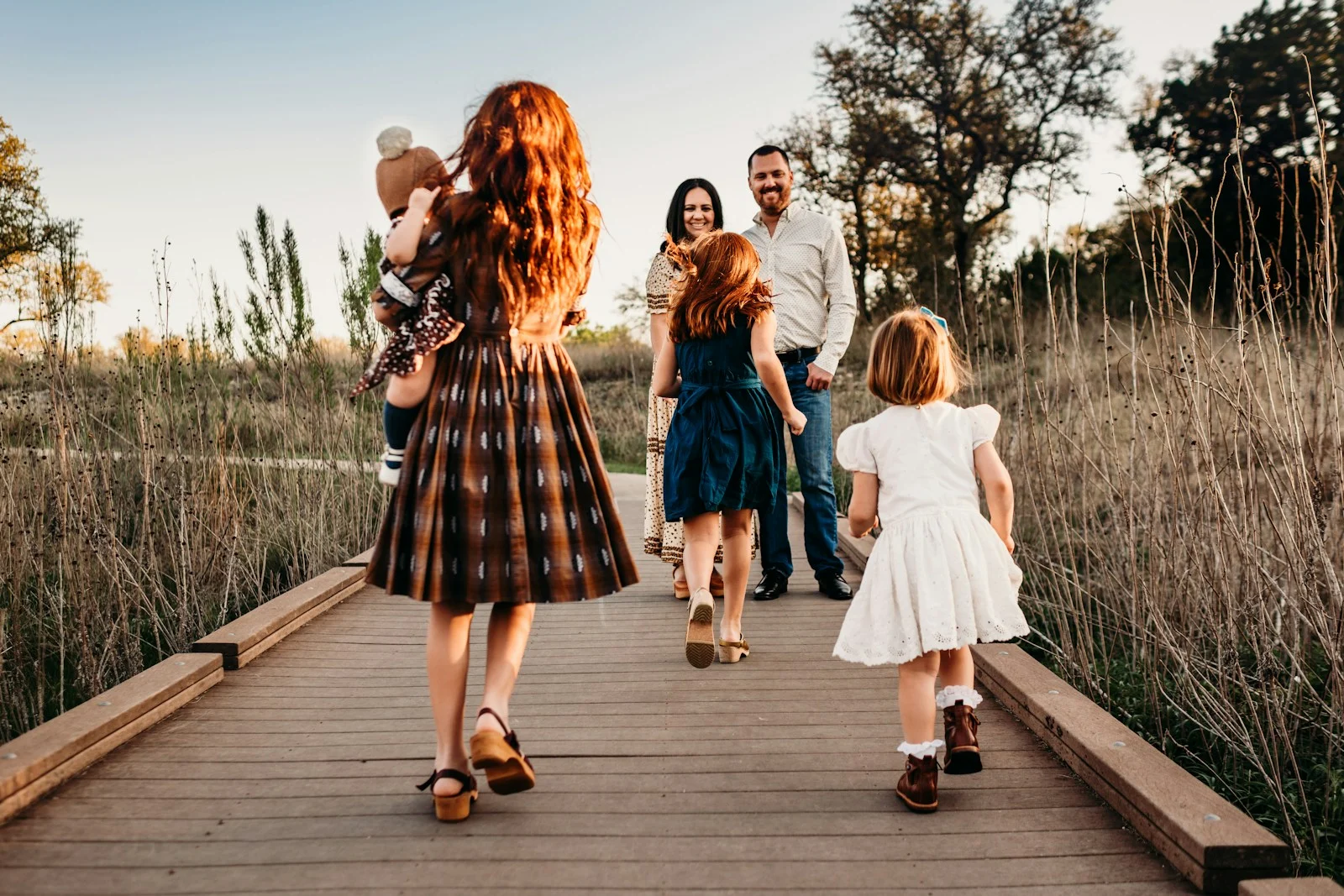 A family walking along a wooden boardwalk in a field during golden hour