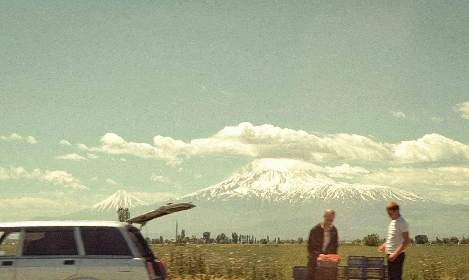 Expatrie : Two men by car with luggage, snowy mountain behind them